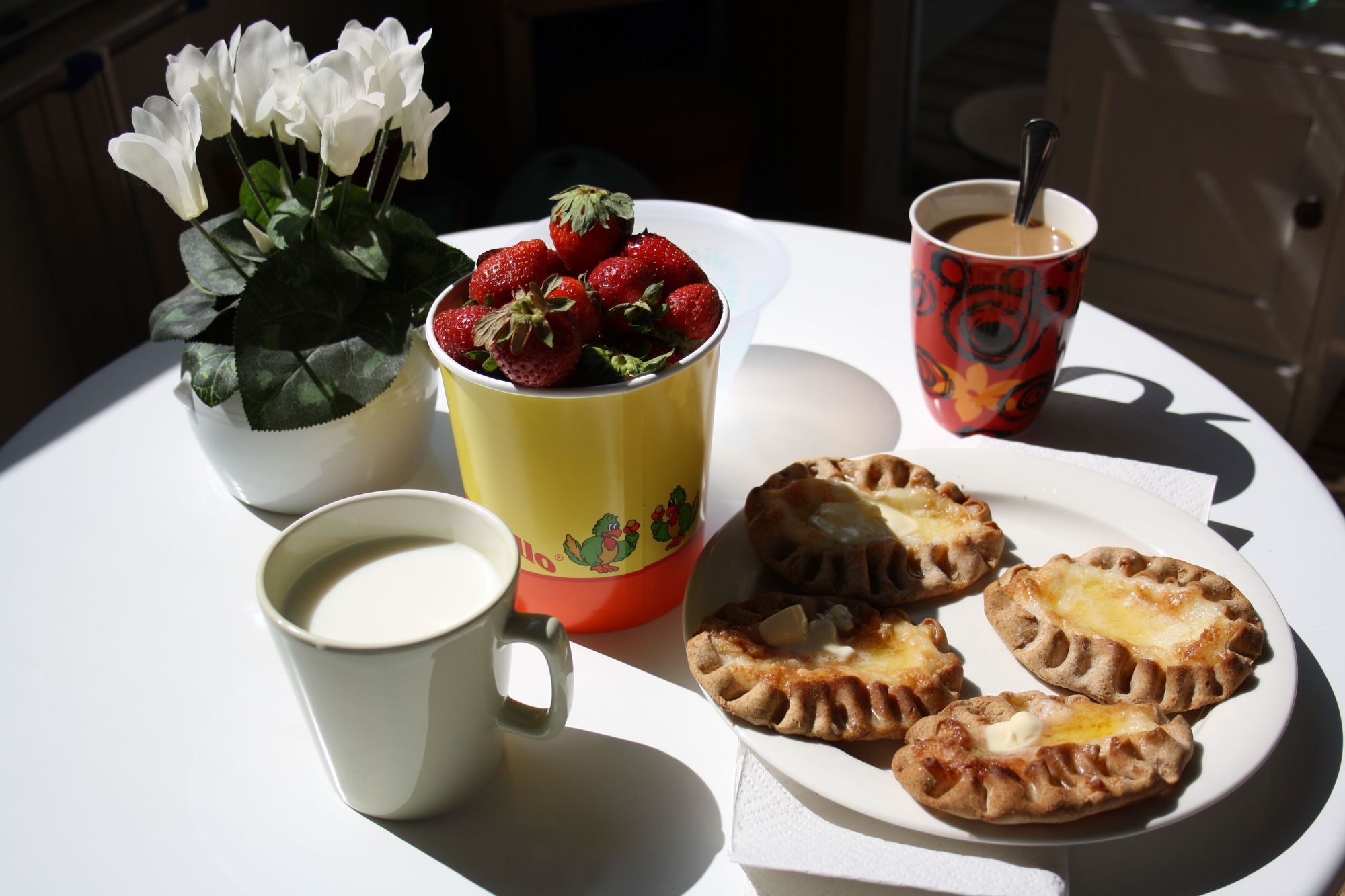 Mesa de desayuno al sol con medialunas, frutillas y café en Almendra