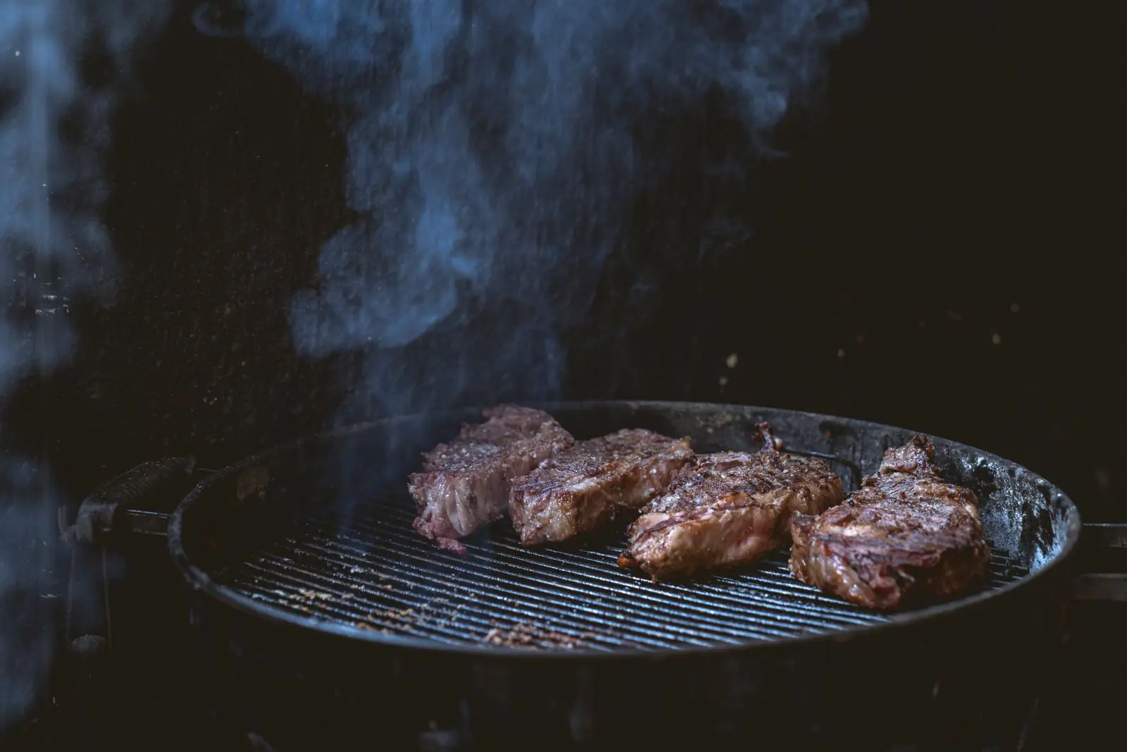 Cortes de carne sobre la parrilla, con humo subiendo en la oscuridad