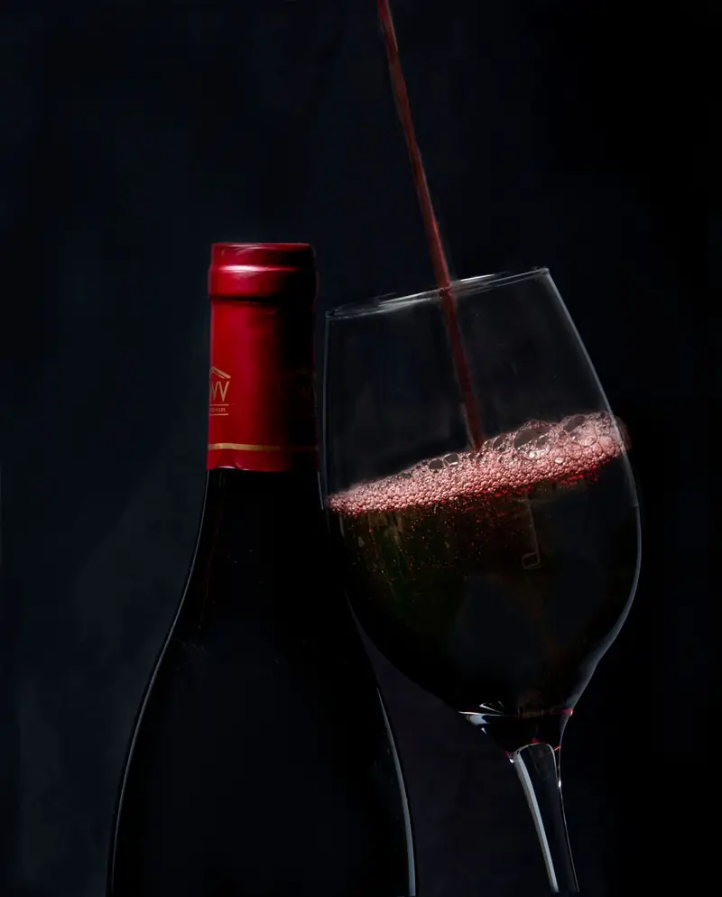 Vino tinto sirviéndose en una copa, sobre fondo oscuro