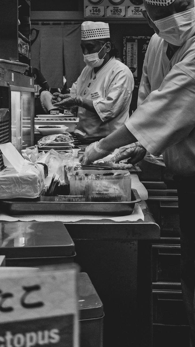 Cocineros preparando sushi en una barra, en blanco y negro